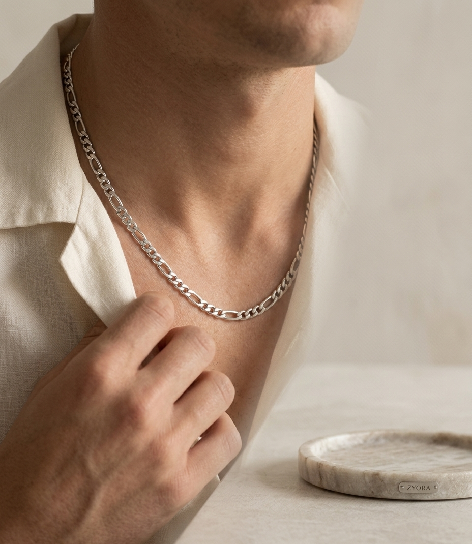 Le Collier Néris homme maille Figaro de couleur argentée en acier inoxydable Zyora tenu entre les doigts pour montrer l'épaisseur et la qualité de finition de l'acier.