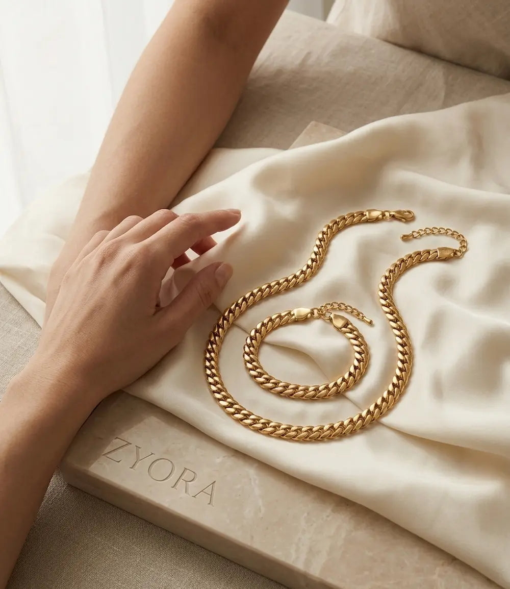 Bracelet porté au poignet et collier Kairo dorés posés sur un tissu, parure de bijoux waterproof maille cubaine