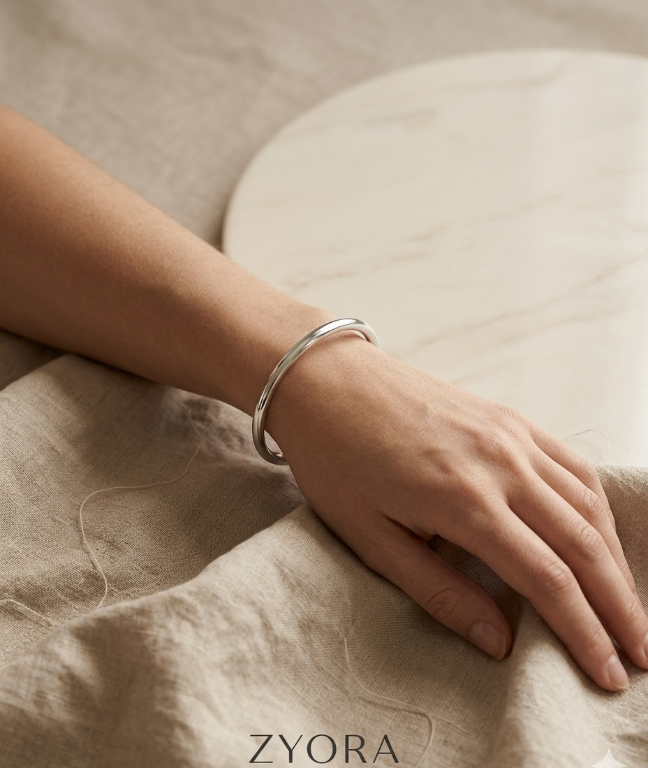 Bracelet ouvert de couleur argenté Sora porté au poignet et posé sur un tissu, bijou waterproof Zyora